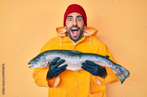Handsome hispanic man with beard wearing fisherman equipment celebrating crazy and amazed for success with open eyes screaming excited.