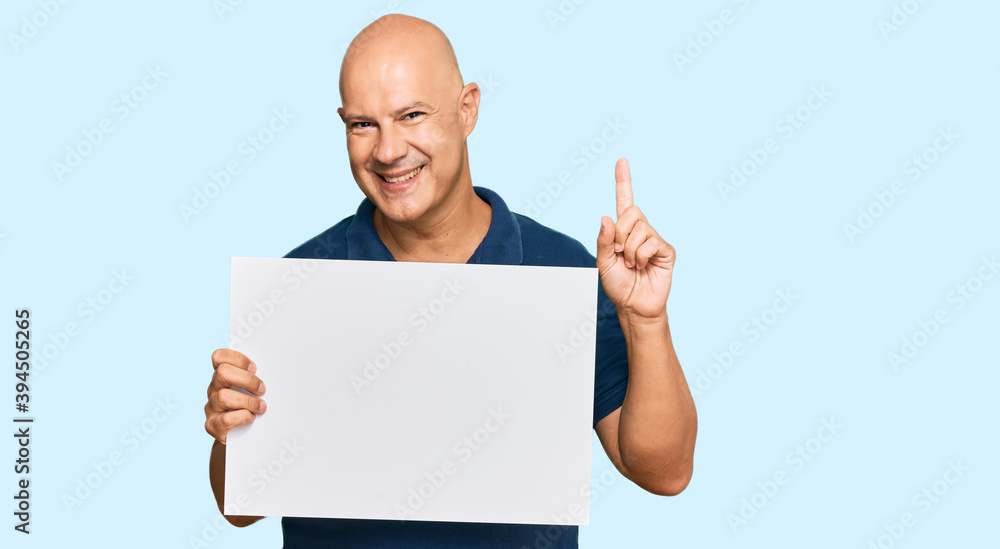 Middle age bald man holding blank empty banner surprised with an idea or question pointing finger with happy face, number one Middle age bald man holding blank empty banner surprised with an idea or question pointing finger with happy face, number one