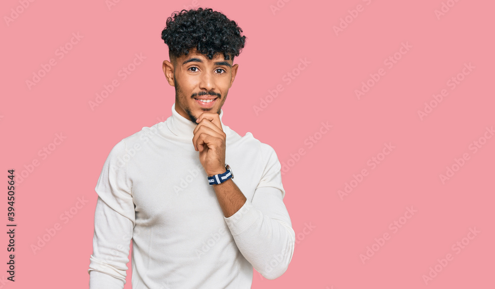 Young arab man wearing casual winter sweater looking confident at the camera smiling with crossed arms and hand raised on chin. thinking positive. Young arab man wearing casual winter sweater looking confident at the camera smiling with crossed arms and hand raised on chin. thinking positive.