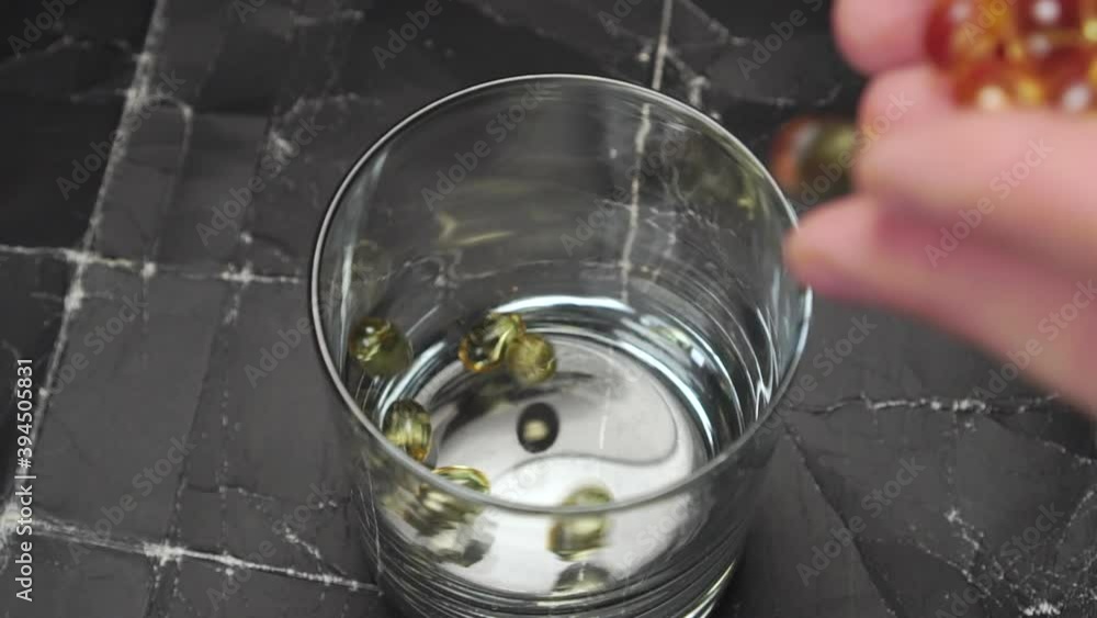 Omega 3 pills are falling from hands into a glass on an old grunge dark background. Slow motion. Close-up Omega 3 pills are falling from hands into a glass on an old grunge dark background. Slow motion. Close-up
