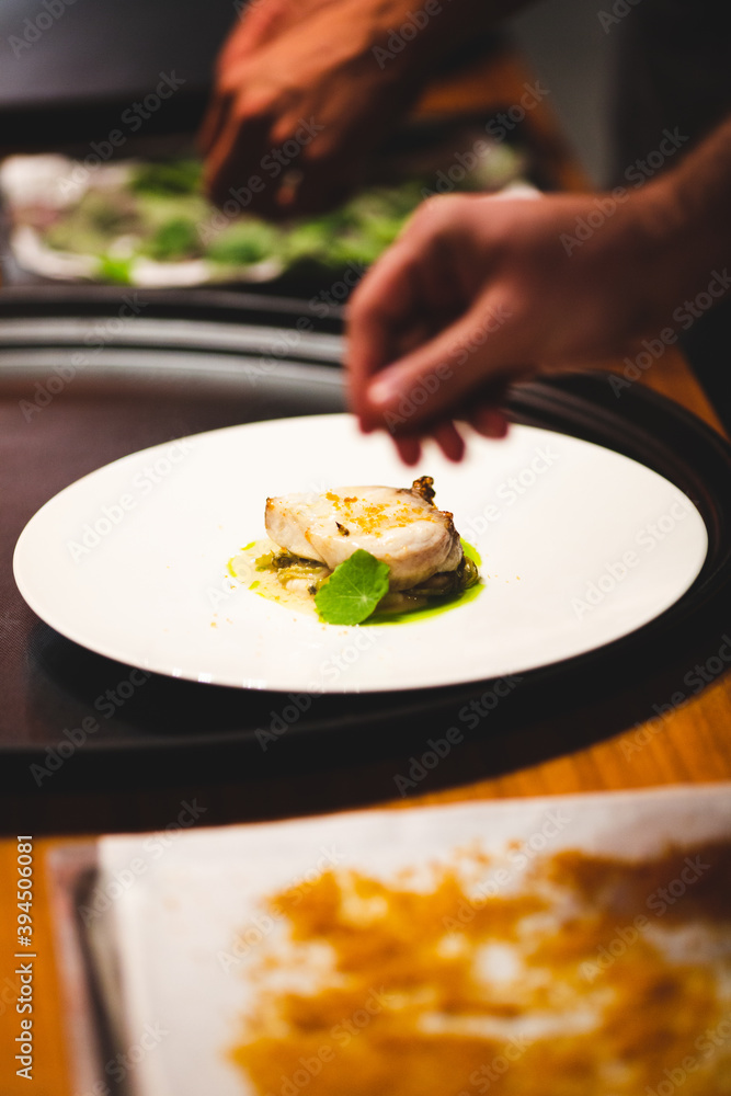 Professional cook puts salt and green ingredients in fish dish Professional cook puts salt and green ingredients in fish dish