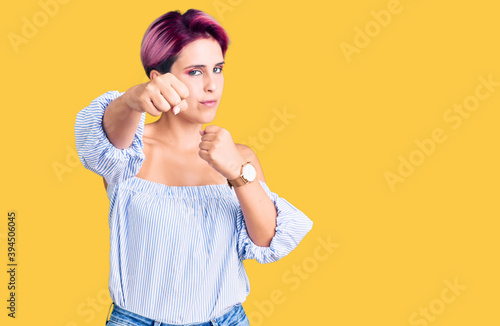 Young beautiful woman with pink hair wearing casual clothes punching fist to fight, aggressive and angry attack, threat and violence