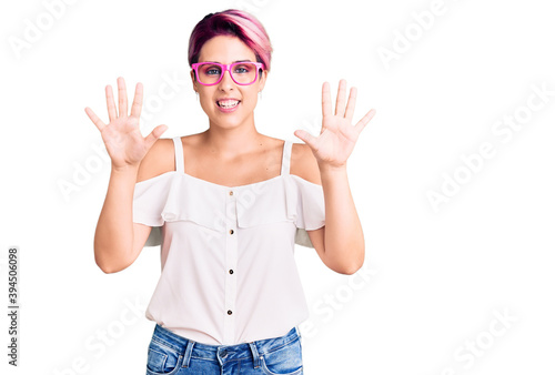 Young beautiful woman with pink hair wearing casual clothes and glasses showing and pointing up with fingers number ten while smiling confident and happy.