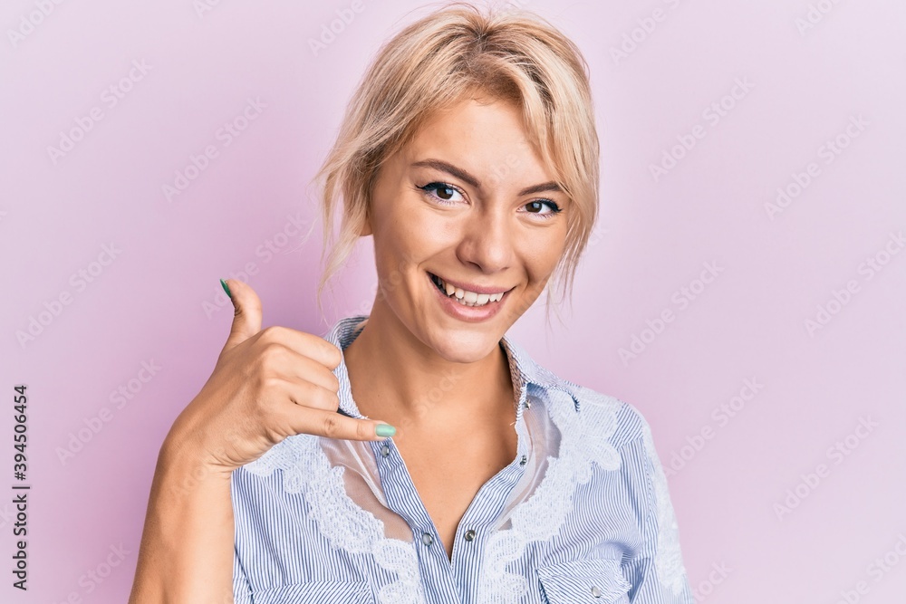Young blonde girl wearing casual clothes smiling doing phone gesture with hand and fingers like talking on the telephone. communicating concepts. Young blonde girl wearing casual clothes smiling doing phone gesture with hand and fingers like talking on the telephone. communicating concepts.