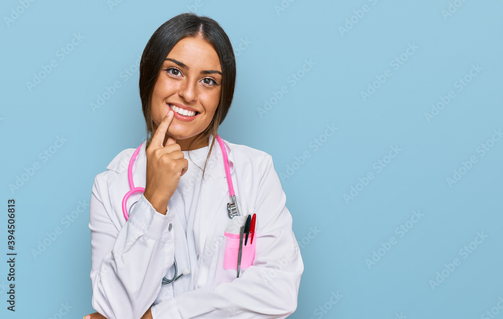 Beautiful hispanic woman wearing doctor uniform and stethoscope looking confident at the camera with smile with crossed arms and hand raised on chin. thinking positive. Beautiful hispanic woman wearing doctor uniform and stethoscope looking confident at the camera with smile with crossed arms and hand raised on chin. thinking positive.