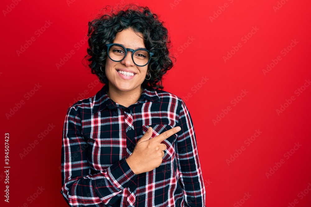 Hispanic woman with curly hair wearing casual clothes and glasses covering ears with fingers with annoyed expression for the noise of loud music. deaf concept. Hispanic woman with curly hair wearing casual clothes and glasses covering ears with fingers with annoyed expression for the noise of loud music. deaf concept.
