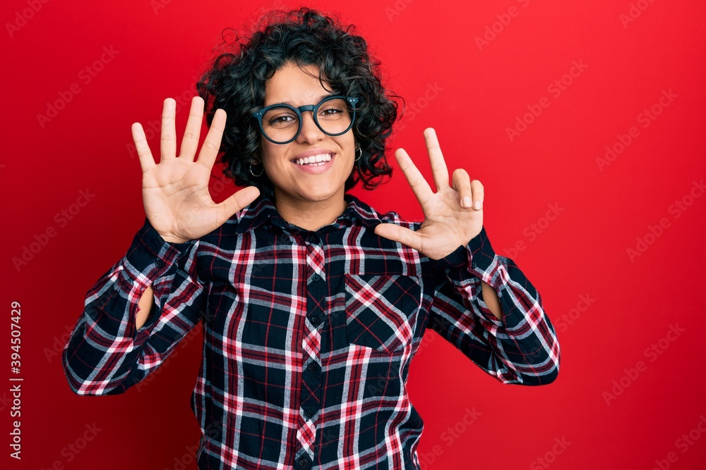 Naklejka premium Hispanic woman with curly hair wearing casual clothes and glasses afraid and terrified with fear expression stop gesture with hands, shouting in shock. panic concept.