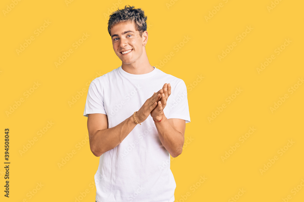 Young handsome man wearing casual white tshirt clapping and applauding happy and joyful, smiling proud hands together Young handsome man wearing casual white tshirt clapping and applauding happy and joyful, smiling proud hands together