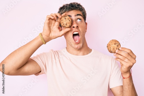 Young handsome man holding cookie angry and mad screaming frustrated and furious, shouting with anger looking up.