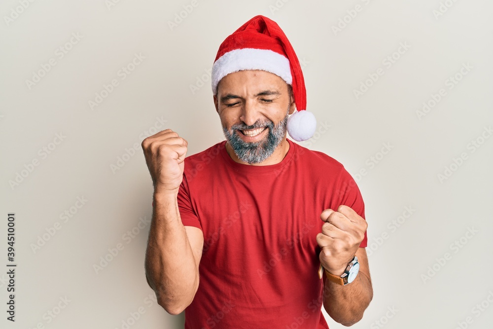 Fototapeta premium Middle age handsome man wearing christmas hat and summer t-shirt celebrating surprised and amazed for success with arms raised and eyes closed