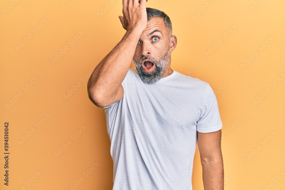 Middle age handsome man wearing casual white tshirt surprised with hand on head for mistake, remember error. forgot, bad memory concept. Middle age handsome man wearing casual white tshirt surprised with hand on head for mistake, remember error. forgot, bad memory concept.