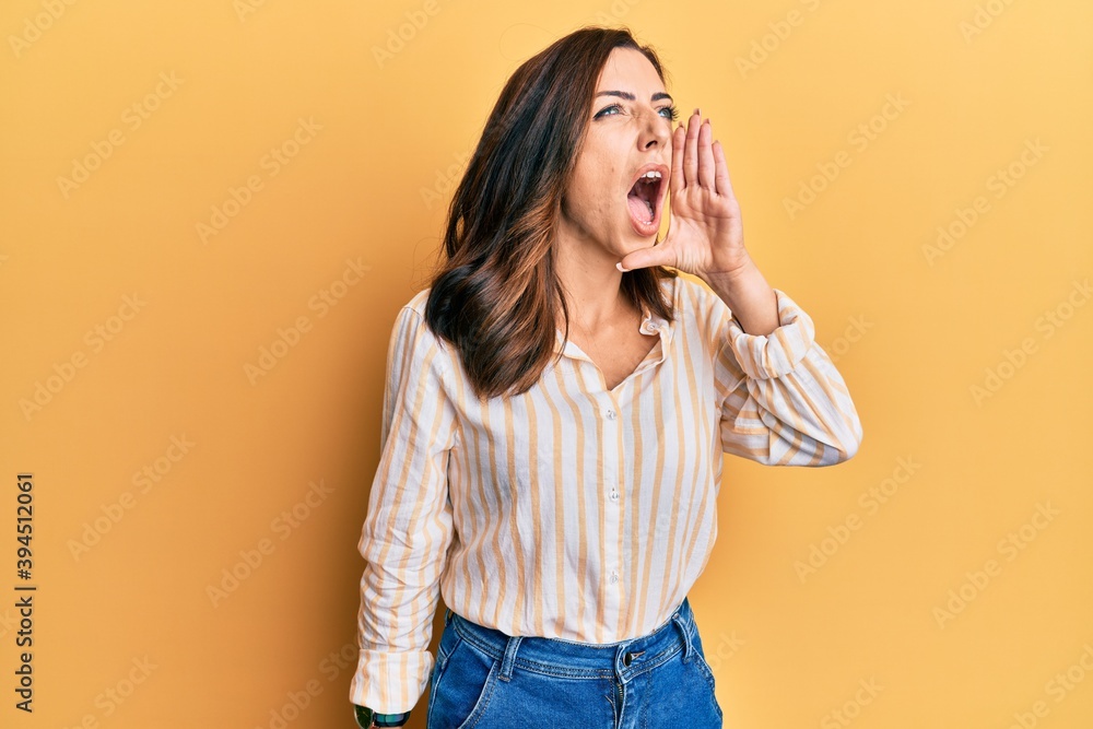Young brunette woman wearing casual clothes over yellow background shouting and screaming loud to side with hand on mouth. communication concept. Young brunette woman wearing casual clothes over yellow background shouting and screaming loud to side with hand on mouth. communication concept.