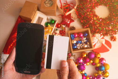 Man hands holding credit card and using smartphone by festive xmas presents and decor, close-up. christmas online shopping