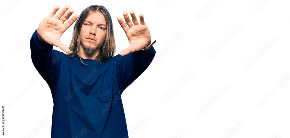 Handsome caucasian man with long hair wearing casual winter sweater doing frame using hands palms and fingers, camera perspective Handsome caucasian man with long hair wearing casual winter sweater doing frame using hands palms and fingers, camera perspective