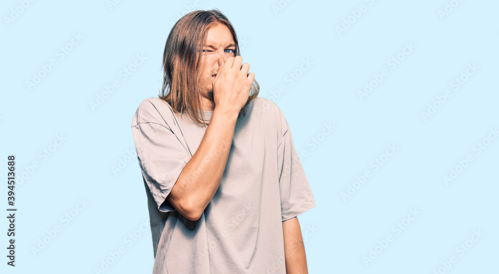 Handsome caucasian man with long hair wearing casual clothes smelling something stinky and disgusting, intolerable smell, holding breath with fingers on nose. bad smell Handsome caucasian man with long hair wearing casual clothes smelling something stinky and disgusting, intolerable smell, holding breath with fingers on nose. bad smell