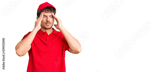 Young handsome man with curly hair wearing delivery uniform suffering from headache desperate and stressed because pain and migraine. hands on head.