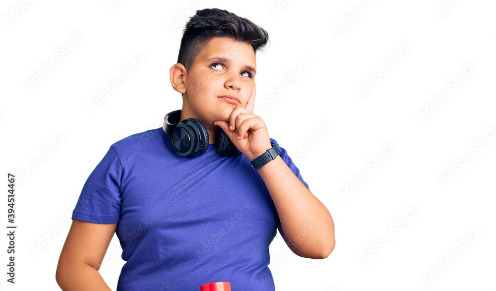 Little boy kid holding skate and wearing headphones serious face thinking about question with hand on chin, thoughtful about confusing idea Little boy kid holding skate and wearing headphones serious face thinking about question with hand on chin, thoughtful about confusing idea