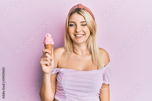Young caucasian woman holding ice cream winking looking at the camera with sexy expression, cheerful and happy face.
