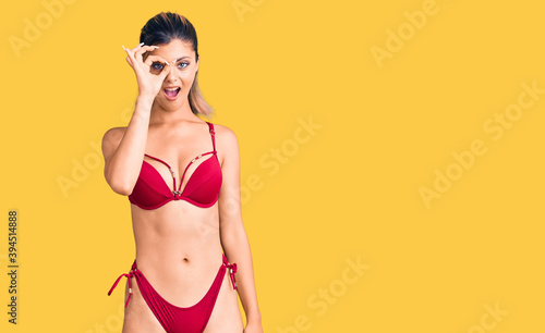 Young beautiful woman wearing bikini doing ok gesture shocked with surprised face, eye looking through fingers. unbelieving expression. © Krakenimages.com