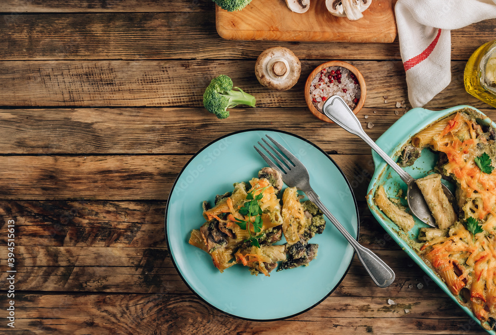 Casserole with pasta, mushrooms, broccoli sauce and cheese on a rustic wooden background.