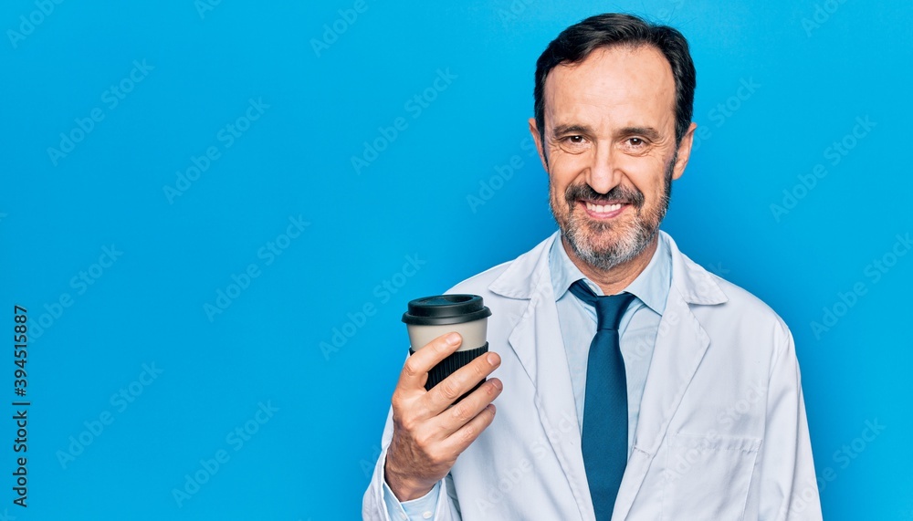 Middle age handsome doctor man wearing coat drinking cup of takeaway coffee looking positive and happy standing and smiling with a confident smile showing teeth Middle age handsome doctor man wearing coat drinking cup of takeaway coffee looking positive and happy standing and smiling with a confident smile showing teeth