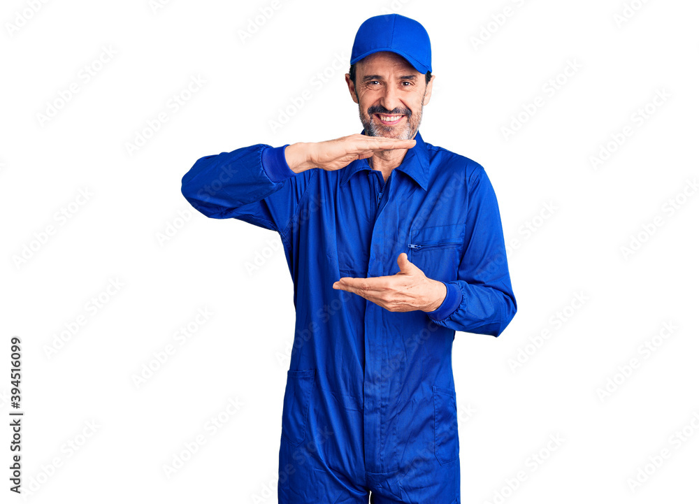 Middle age handsome man wearing mechanic uniform gesturing with hands showing big and large size sign, measure symbol. smiling looking at the camera. measuring concept. Middle age handsome man wearing mechanic uniform gesturing with hands showing big and large size sign, measure symbol. smiling looking at the camera. measuring concept.
