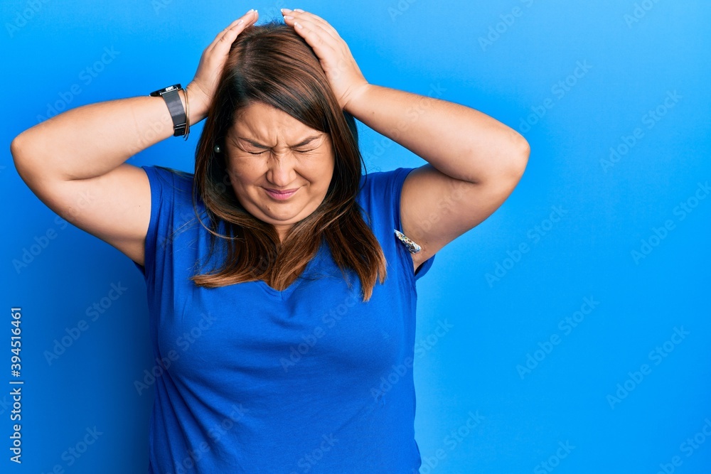 Beautiful hispanic plus size woman wearing casual blue t shirt covering one eye with hand, confident smile on face and surprise emotion. Beautiful hispanic plus size woman wearing casual blue t shirt covering one eye with hand, confident smile on face and surprise emotion.