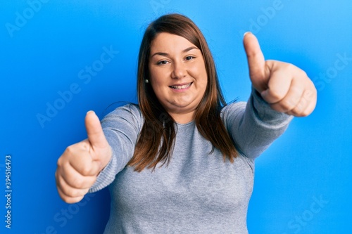 Beautiful hispanic plus size woman wearing casual clothes showing and pointing up with finger number one while smiling confident and happy. © Krakenimages.com
