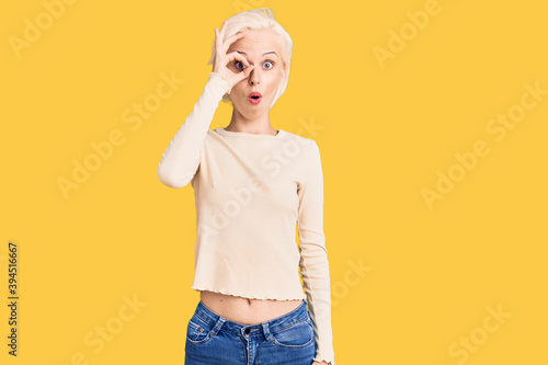Young blonde woman wearing casual clothes doing ok gesture shocked with surprised face, eye looking through fingers. unbelieving expression.
