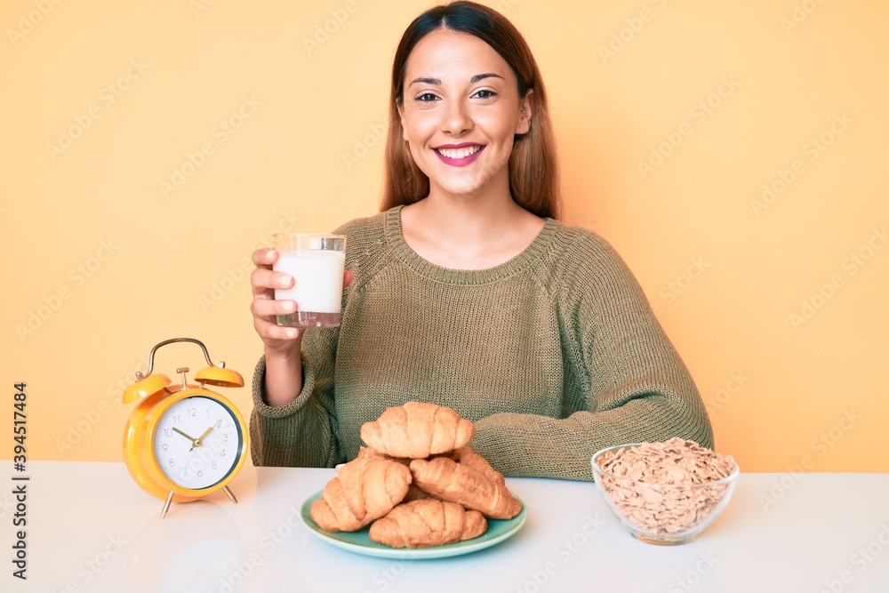 Young brunette woman drinking a glass of milk for breakfast looking positive and happy standing and smiling with a confident smile showing teeth Young brunette woman drinking a glass of milk for breakfast looking positive and happy standing and smiling with a confident smile showing teeth