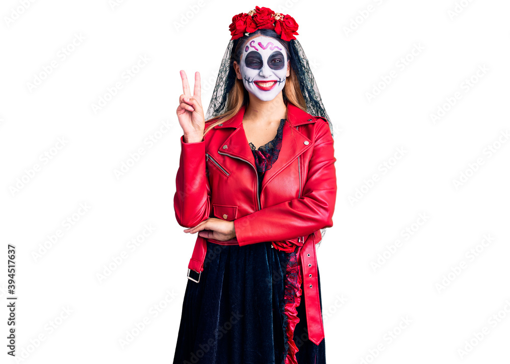 Woman wearing day of the dead costume over background smiling with happy face winking at the camera doing victory sign. number two.