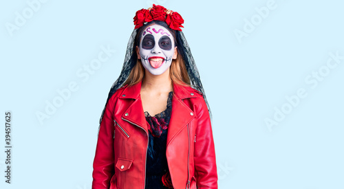 Woman wearing day of the dead costume over background sticking tongue out happy with funny expression. emotion concept.