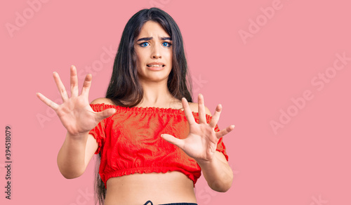 Brunette teenager girl wearing casual clothes afraid and terrified with fear expression stop gesture with hands, shouting in shock. panic concept.