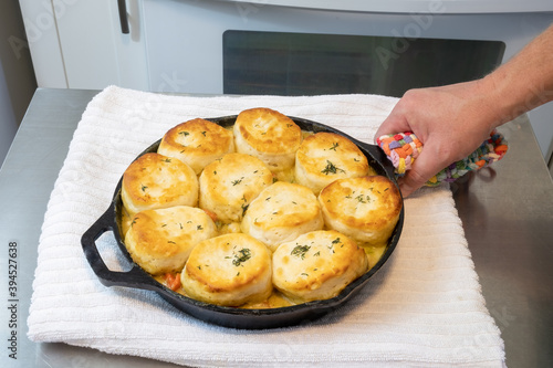 Chicken pot pie with biscuits used on top cooked to a toasty golden brown in a cast iron skillet with a man's hand holding it.