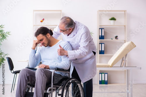 Young man in wheel-chair and old doctor traumatologist