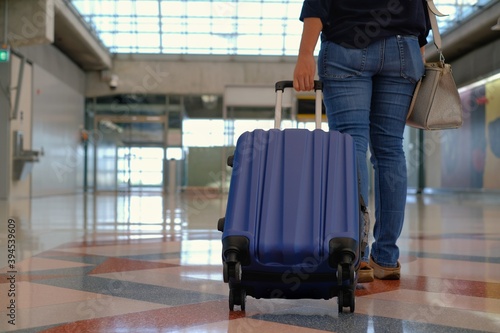 A back view, lower half body shot of a woman in jeans, walking in an airport terminal, pulling her blue suitcase along in the back, getting ready to board her airplane.