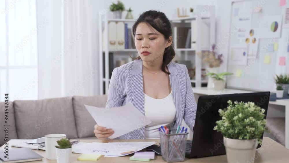 professional asian taiwanese woman employee in blazer is working on financial statement and having coffee in the home office. professional asian taiwanese woman employee in blazer is working on financial statement and having coffee in the home office.