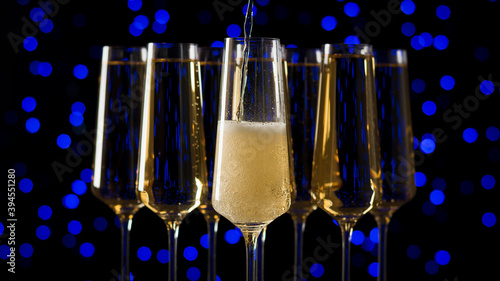 Filling one of the five glasses with sparkling wine on a blue bokeh background.