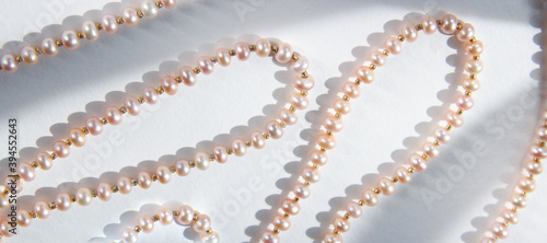 Pink pearl necklace background with hard shadows. Top view.