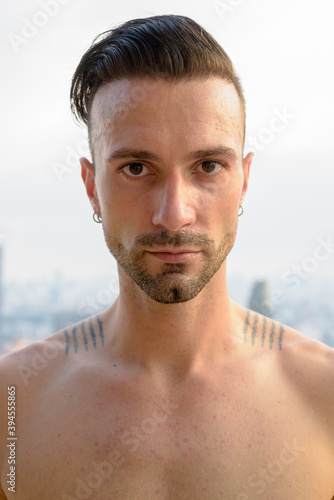 Portrait of handsome young man shirtless outdoors at rooftop in city