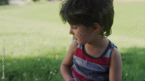 Close-up of a young boy talking and playing with his mother while laying on the park grass