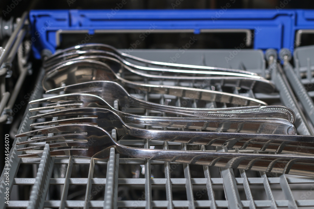 A man loads dirty dishes, plates, spoons, forks, cutlery into dishwasher tray. A man loads dirty dishes, plates, spoons, forks, cutlery into dishwasher tray.