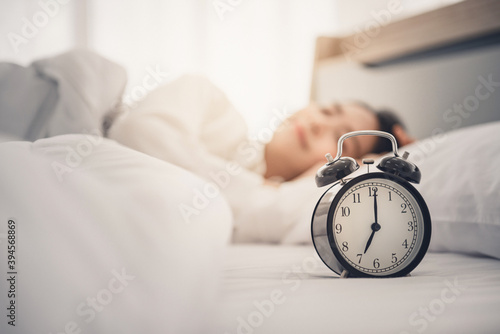 Young woman sleeping on bed with alarm clock in morning.