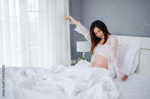pregnant woman waking up on the bed in morning and stretching herself