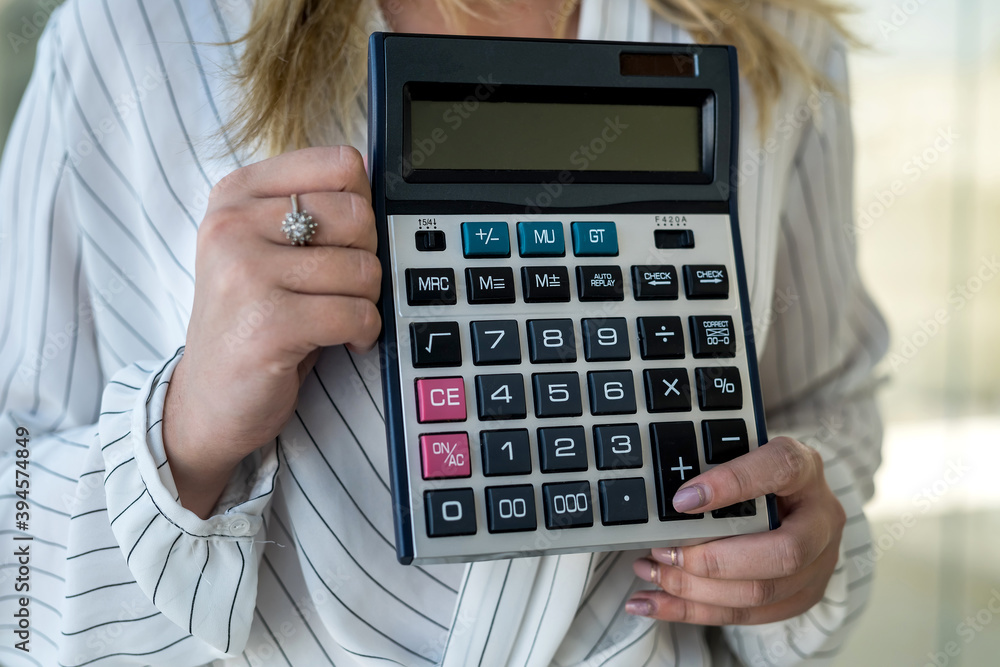 Close-up of female hand holding calculator over modern center as background Close-up of female hand holding calculator over modern center as background