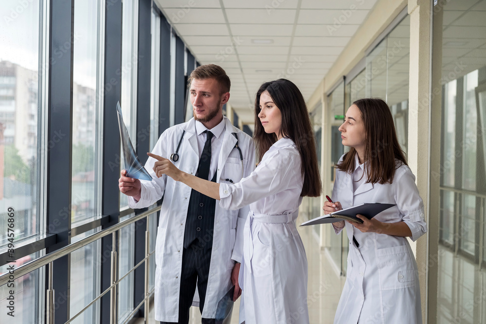 Three young doctors discusses the results of an MRI scan of the patient's head in modern hospital hallway. Three young doctors discusses the results of an MRI scan of the patient's head in modern hospital hallway.