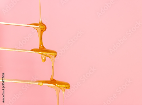 Sugar paste for hair removal runs down a wooden spatula. The concept of depilation, waxing and sugaring. Pink background, free space for text.