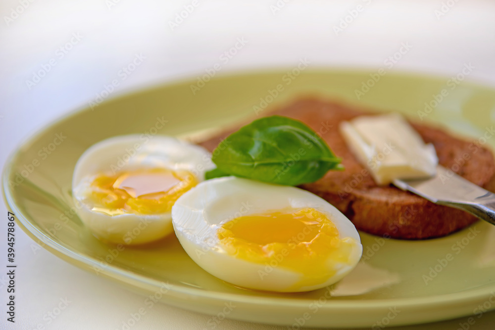 Two soft-boiled egg halves on a plate. Basil leaf, toast and butter. Close up. Two soft-boiled egg halves on a plate. Basil leaf, toast and butter. Close up.