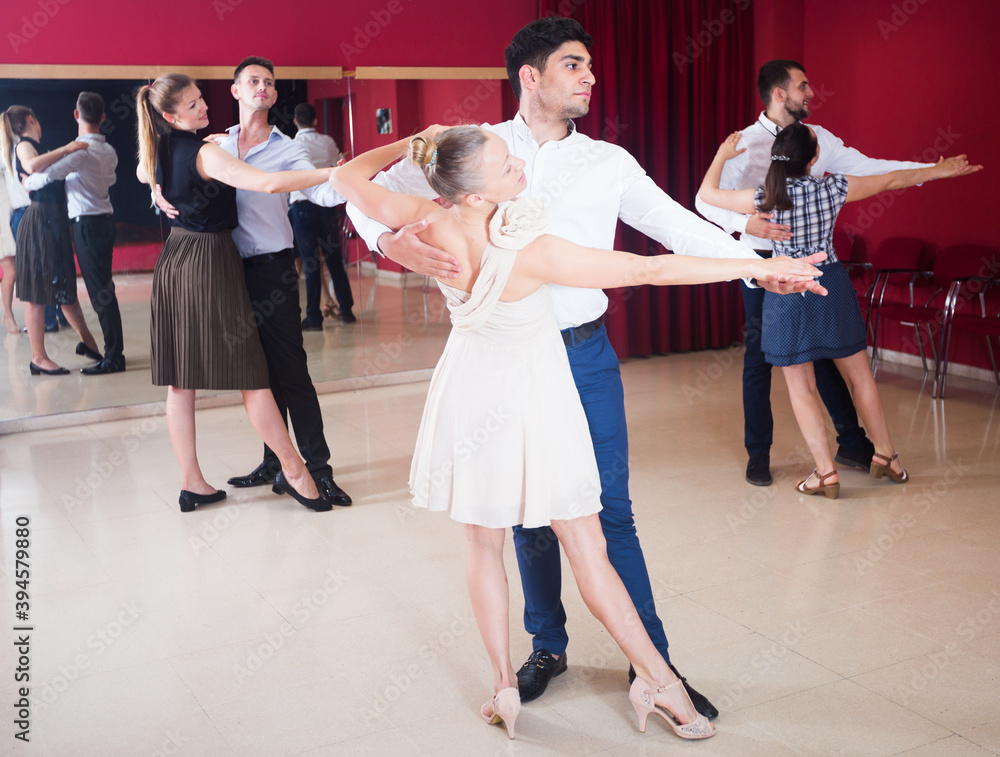 Young smiling people learning to dance waltz in dancing class