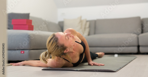 Beautiful blonde woman doing home workout indoors. Woman practice yoga at home. Fit girl using workout tutorials for healthy active lifestyle. Woman using quarantine for home workouts. Stretching